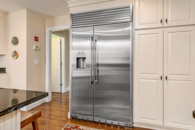 kitchen featuring baseboards, stainless steel built in fridge, dark stone countertops, white cabinets, and dark wood-style flooring