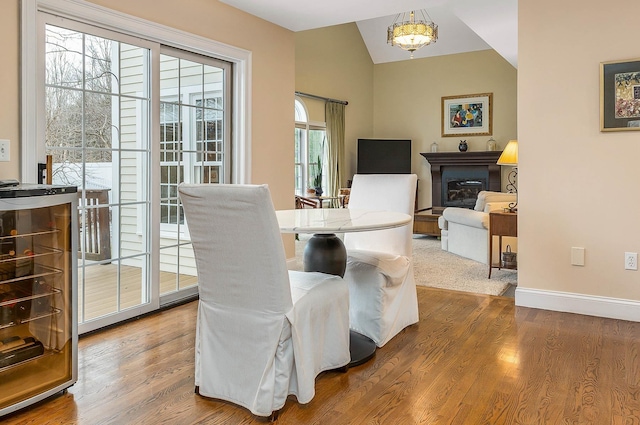 dining space with wood finished floors, wine cooler, a fireplace, baseboards, and vaulted ceiling