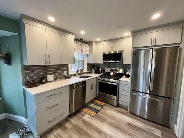 kitchen with appliances with stainless steel finishes, light wood-type flooring, light countertops, and a sink