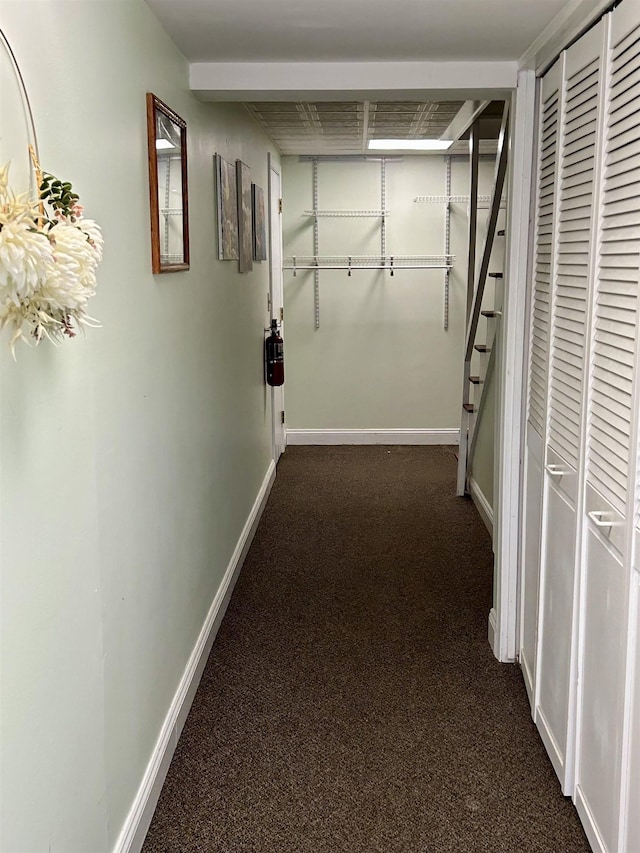 hallway with stairs, baseboards, and dark colored carpet