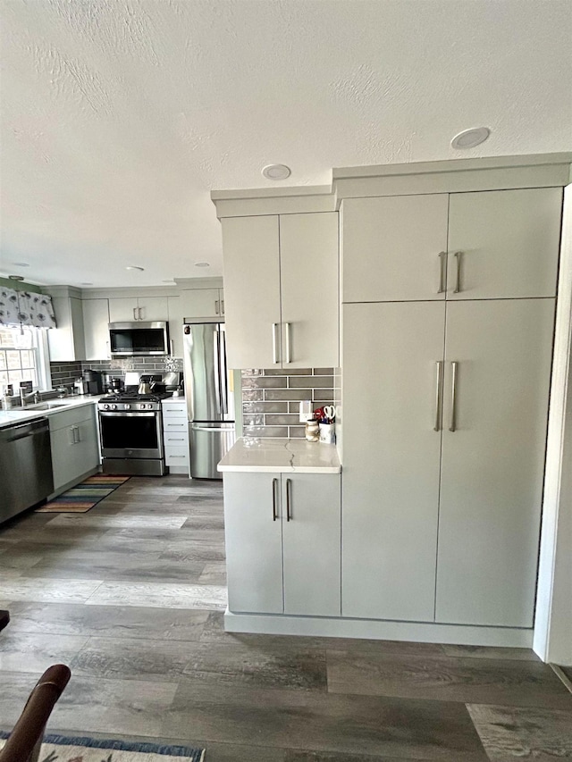 kitchen with stainless steel appliances, tasteful backsplash, wood finished floors, and light countertops