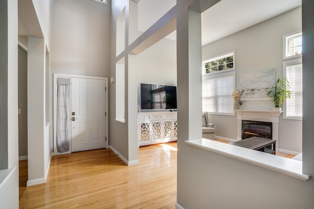 foyer with a glass covered fireplace, baseboards, a high ceiling, and light wood-style floors