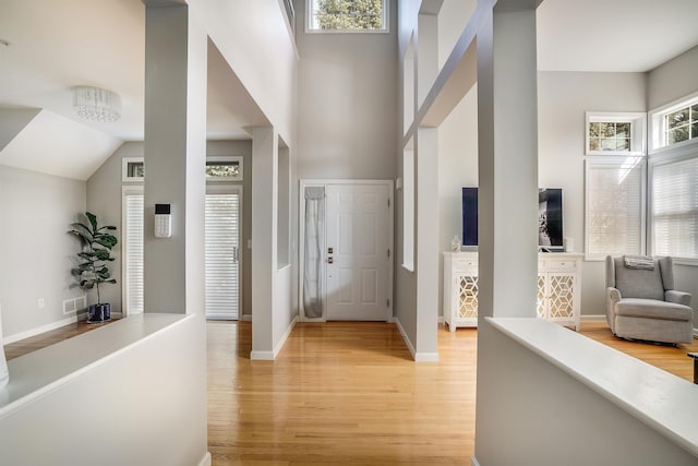 foyer entrance featuring visible vents, baseboards, light wood-style floors, and a towering ceiling