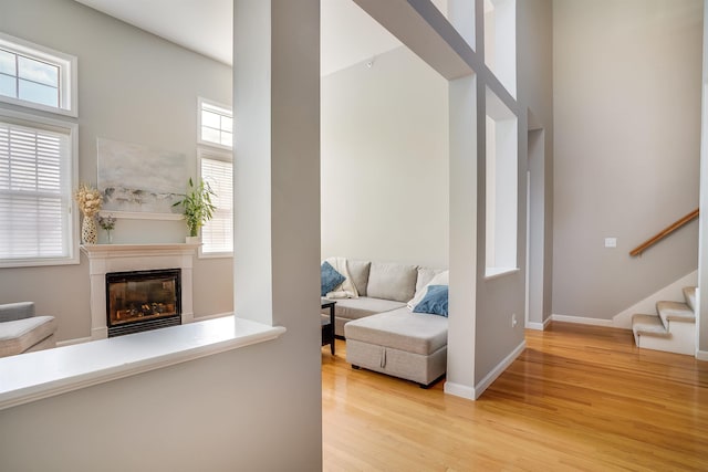 living room with a glass covered fireplace, stairway, light wood-style floors, and baseboards