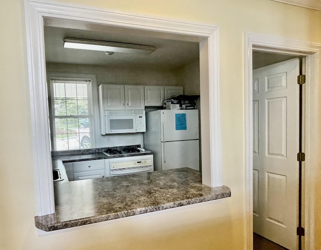 kitchen with dark countertops, white appliances, white cabinetry, and a peninsula