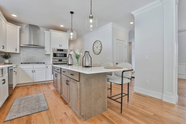 kitchen with crown molding, wall chimney range hood, light wood-type flooring, a kitchen bar, and decorative backsplash