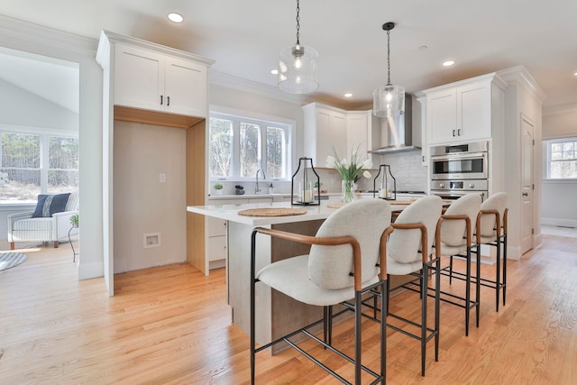 kitchen with a center island with sink, light countertops, ornamental molding, light wood-style flooring, and white cabinetry