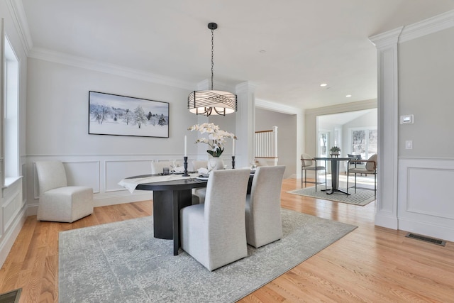 dining space featuring visible vents, a decorative wall, wood finished floors, and ornamental molding