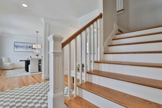 stairway with wood finished floors, recessed lighting, ornamental molding, wainscoting, and a decorative wall