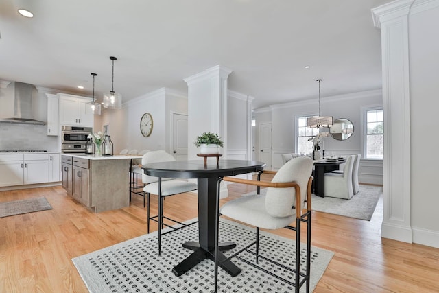 dining room featuring a wainscoted wall, light wood-type flooring, and decorative columns