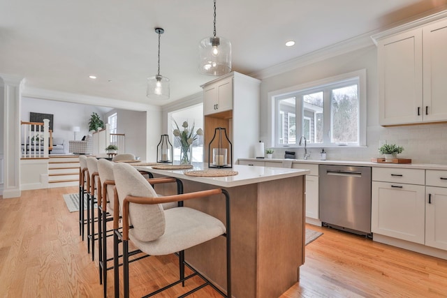 kitchen with a kitchen island, crown molding, a kitchen bar, light wood-style flooring, and stainless steel dishwasher