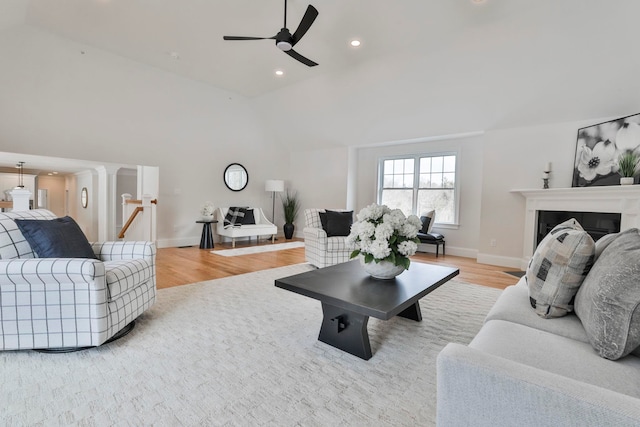 living room with baseboards, light wood-type flooring, lofted ceiling, a fireplace, and a ceiling fan