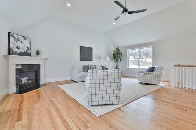 living area with a ceiling fan, wood finished floors, baseboards, lofted ceiling, and a fireplace with flush hearth