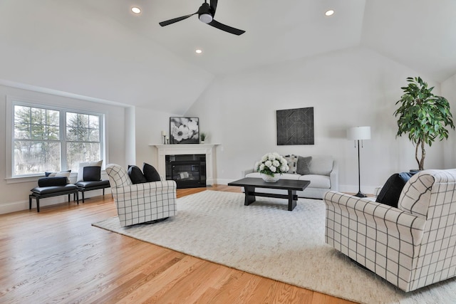 living room featuring a glass covered fireplace, wood finished floors, baseboards, ceiling fan, and vaulted ceiling