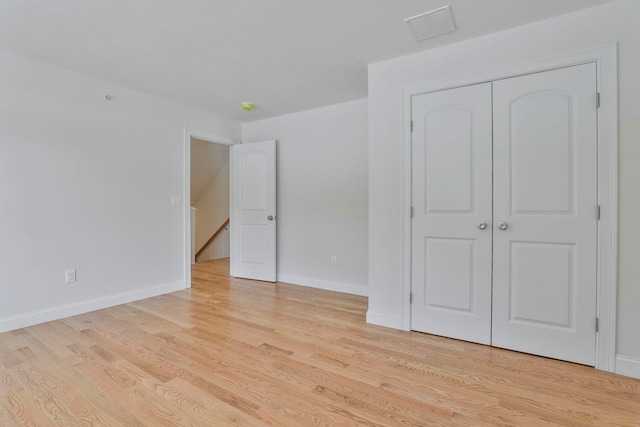 unfurnished bedroom with light wood-style flooring, baseboards, visible vents, and a closet