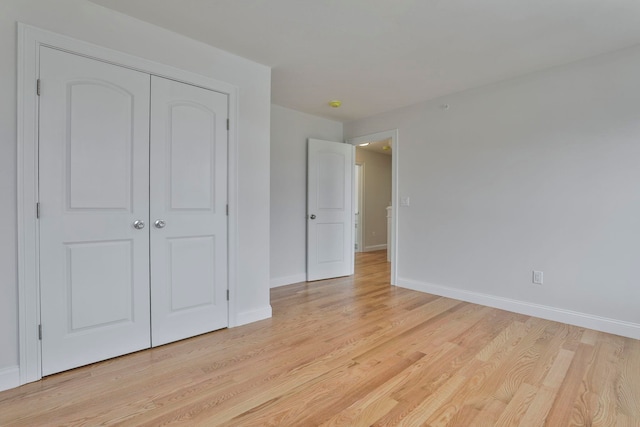 unfurnished bedroom featuring a closet, light wood-type flooring, and baseboards