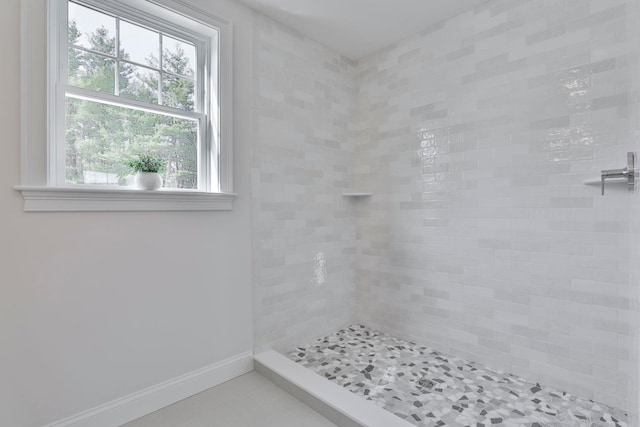 bathroom with tiled shower, baseboards, and tile patterned flooring