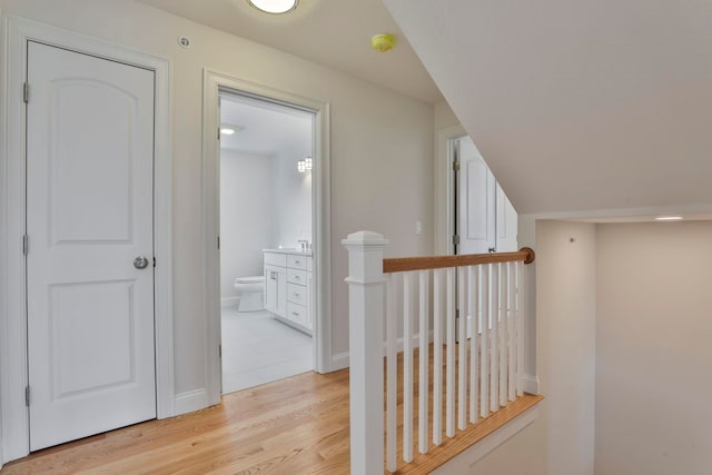 corridor featuring vaulted ceiling, an upstairs landing, light wood-type flooring, and baseboards