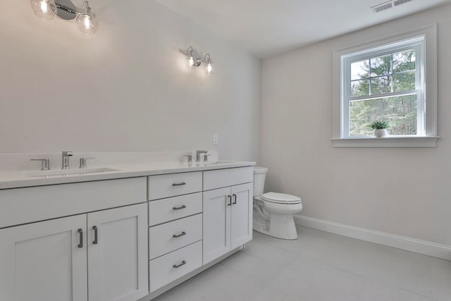 bathroom featuring double vanity, toilet, baseboards, and a sink