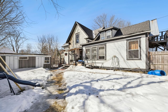 snow covered house with an outdoor structure and fence