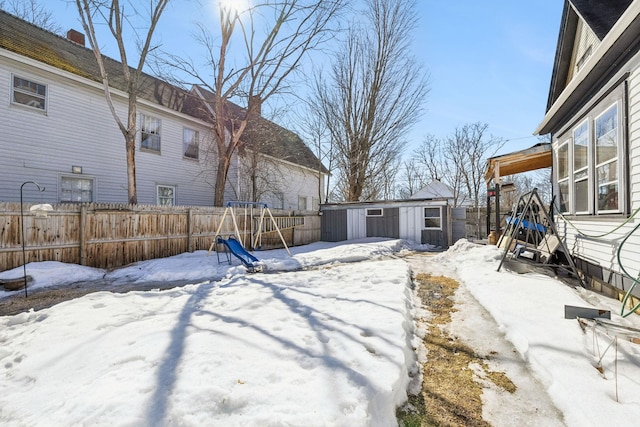 snowy yard featuring a playground, an outbuilding, and fence