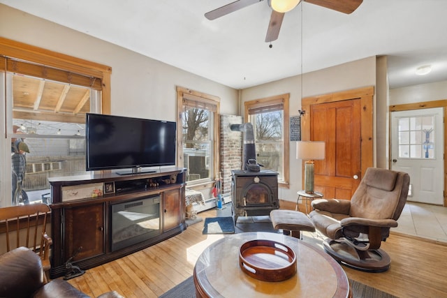 living room with a wood stove, light wood-style flooring, and ceiling fan