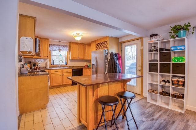 kitchen featuring a sink, decorative backsplash, stainless steel refrigerator with ice dispenser, a kitchen breakfast bar, and a center island