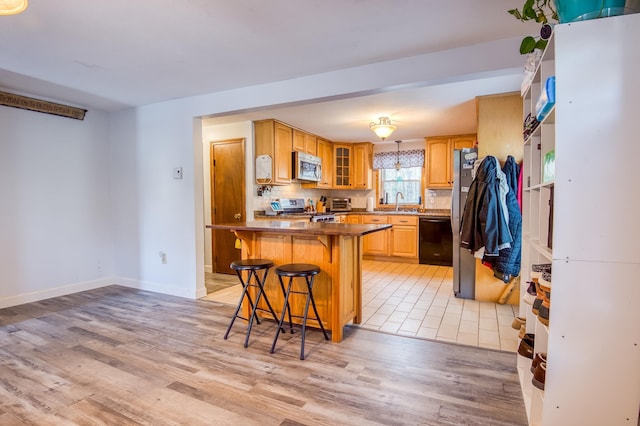 kitchen featuring light wood-type flooring, backsplash, appliances with stainless steel finishes, a breakfast bar area, and glass insert cabinets