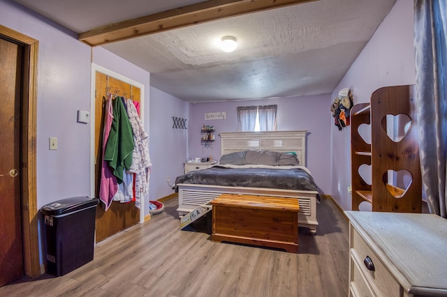 bedroom with beam ceiling, a textured ceiling, and wood finished floors