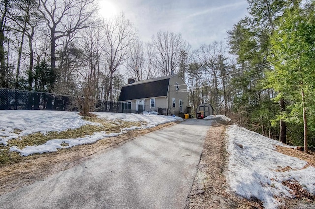 view of front of property featuring an outbuilding, fence, a gambrel roof, a chimney, and aphalt driveway