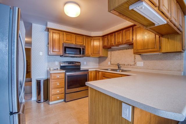 kitchen with wallpapered walls, light countertops, light tile patterned floors, appliances with stainless steel finishes, and a sink