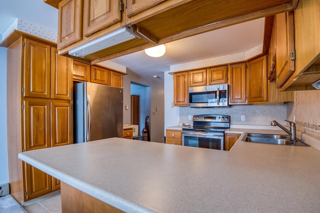 kitchen featuring decorative backsplash, a peninsula, appliances with stainless steel finishes, and a sink