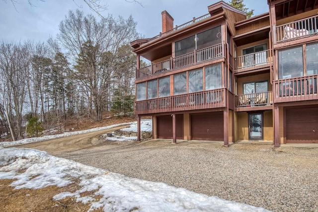 snow covered property featuring an attached garage, a chimney, and driveway