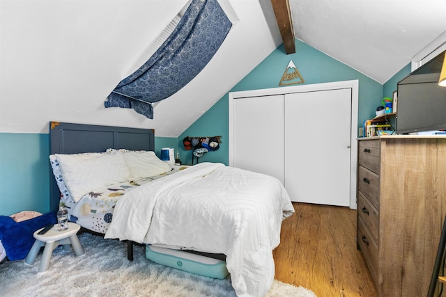 bedroom with a closet, wood finished floors, and vaulted ceiling with beams