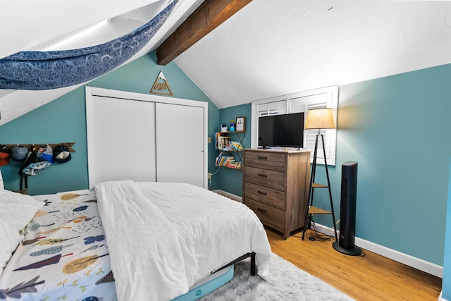 bedroom with light wood finished floors, a closet, vaulted ceiling with beams, and baseboards