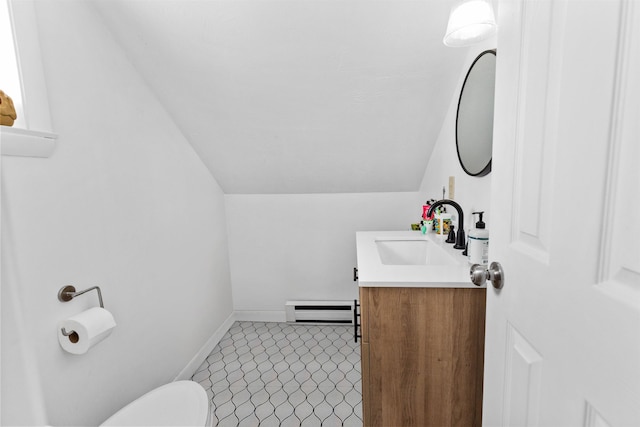 half bath with toilet, a baseboard radiator, baseboards, vanity, and vaulted ceiling