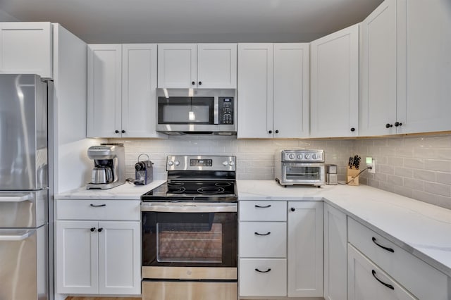 kitchen with backsplash, white cabinetry, stainless steel appliances, and light stone countertops