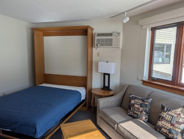 bedroom with an AC wall unit, track lighting, and a textured ceiling