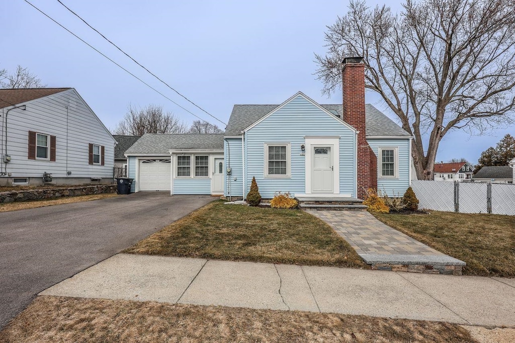 view of front of home with fence, roof with shingles, a chimney, a front lawn, and aphalt driveway