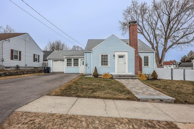 view of front of home with fence, roof with shingles, a chimney, a front lawn, and aphalt driveway