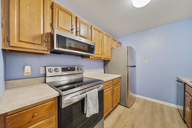 kitchen with baseboards, light countertops, stainless steel appliances, light wood-style floors, and a textured ceiling