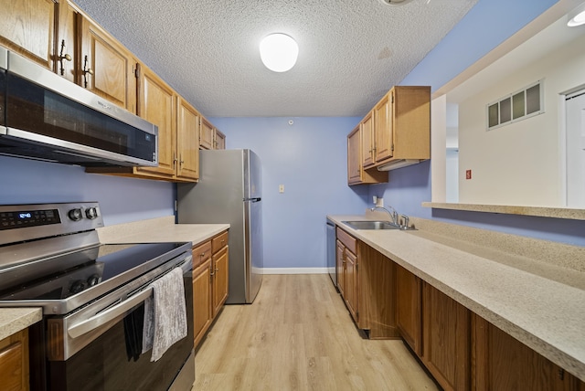 kitchen with light wood-type flooring, a sink, a textured ceiling, appliances with stainless steel finishes, and light countertops