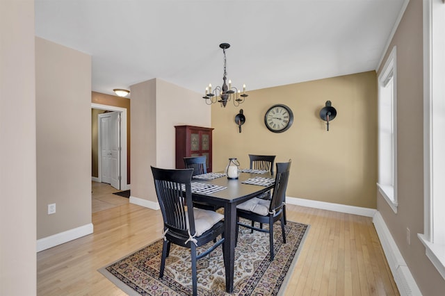 dining space featuring baseboards, a notable chandelier, plenty of natural light, and light wood finished floors