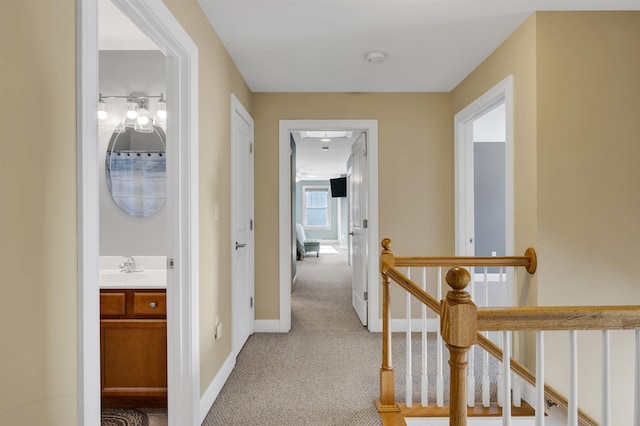 hall featuring a sink, baseboards, light carpet, and an upstairs landing