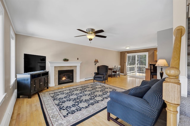 living area with baseboards, ceiling fan, a fireplace with flush hearth, baseboard heating, and light wood-style flooring