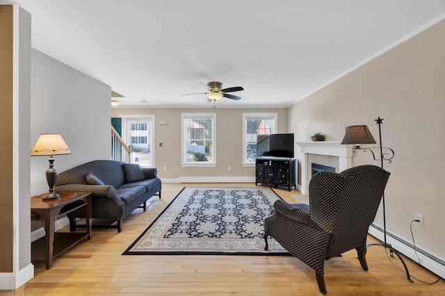 living room featuring a baseboard heating unit, ceiling fan, baseboards, ornamental molding, and light wood-style floors