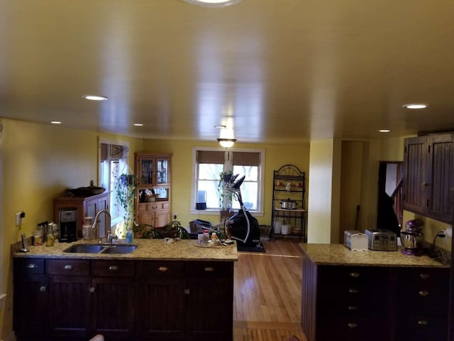 kitchen with dark brown cabinets, light stone countertops, a peninsula, wood finished floors, and a sink