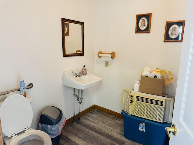 half bathroom with toilet, a wall mounted AC, baseboards, and wood finished floors