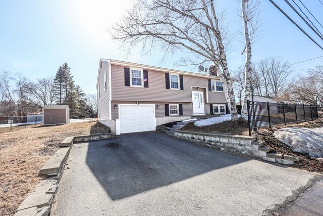 bi-level home featuring aphalt driveway, an attached garage, and fence