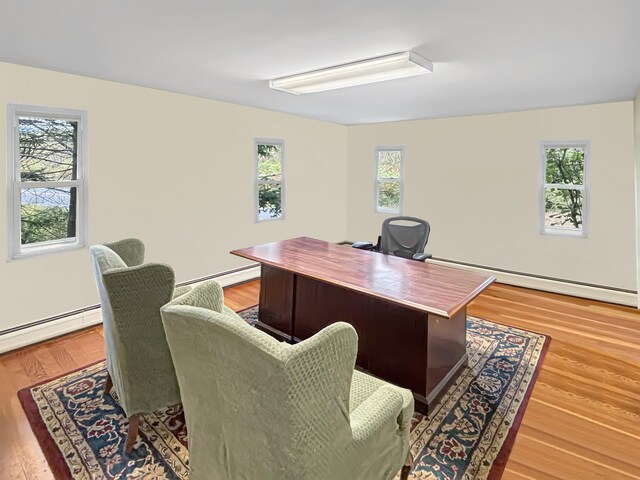 home office featuring a wealth of natural light, baseboard heating, and light wood finished floors